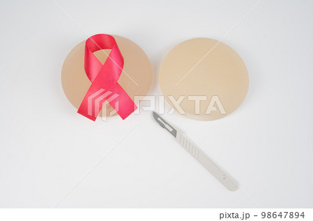 Breast silicone implants, pink tape and a disposable scalpel on a white background. Breast silicone implants, pink tape and a disposable scalpel on a white background. 98647894