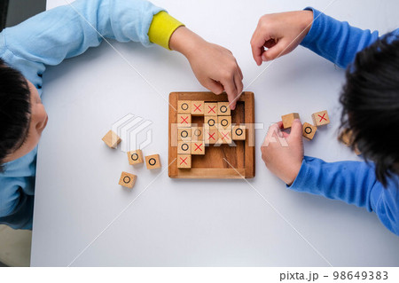 Little siblings playing wooden board game tic-tac-toe on table in living room. Family spending time together on weekend. 98649383