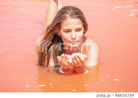 Young woman with long hair in pink salty lake with crystals of salt. Extremely salty pink lake, colored by microalgae with crystalline salt depositions. Spa, beauty and health care concept. 98650784