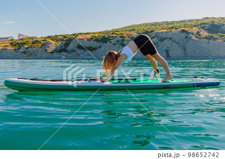 Young woman make yoga or gymnastic on stand up paddle board in quiet sea Young woman make yoga or gymnastic on stand up paddle board in quiet sea 98652742