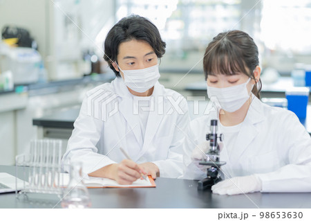 大学の研究室で顕微鏡を見ながら会話をする若い男女 大学の研究室で顕微鏡を見ながら会話をする若い男女 98653630