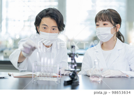 大学の研究室で試験管を見ながら会話をする男女 98653634