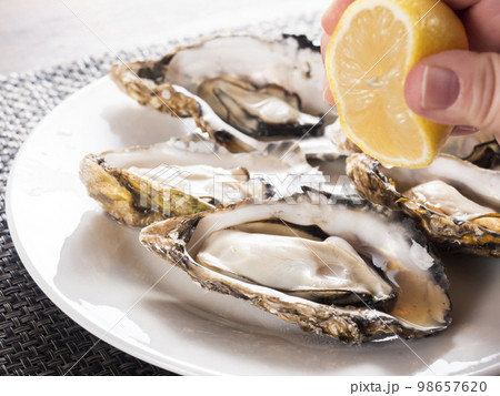 殻付きの蒸し牡蠣にレモンを絞る 殻付きの蒸し牡蠣にレモンを絞る 98657620