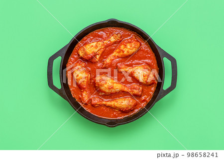 Chicken tomato stew pot, above view on a green background Chicken tomato stew pot, above view on a green background 98658241