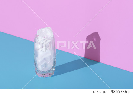 Ice cubes in a glass, in bright light, minimalist on a blue and pink background 98658369