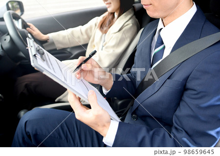 車の運転教習をする男性教官と女性生徒 98659645