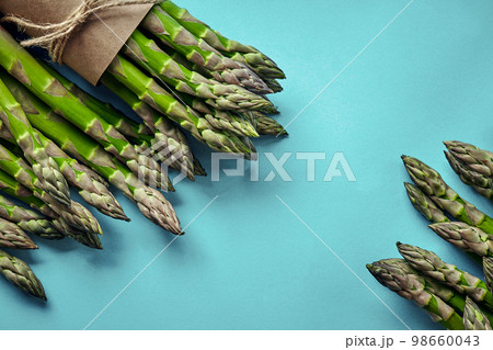 An edible, raw stems of asparagus on blue background. 98660043