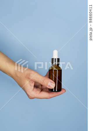 Female hands with serum in bottles on blue background Female hands with serum in bottles on blue background 98660411
