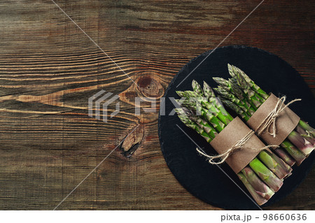 An edible, raw stems of asparagus on a wooden background. An edible, raw stems of asparagus on a wooden background. 98660636