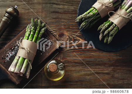 An edible, raw stems of asparagus on a wooden background. 98660678
