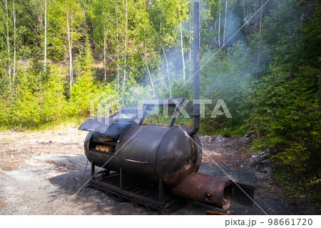 Huge wood smoker stands on the edge of the forest on a sunny day Huge wood smoker stands on the edge of the forest on a sunny day 98661720