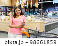Happy caucasian woman using mobile phone in grocery shopping. Checklist application buying food products in supermarket. 98661859