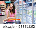 Young smiling woman 20s wearing casual clothes shopping at supermarket standing near in grocery cart talking on mobile phone inside hypermarket. 98661862