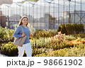 A young pretty woman walks down the street near the large greenhouses. A woman goes to buy green plants for decoration. Landscaping concept 98661902
