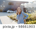 A young pretty girl, dressed in shirt and jeans, stands near the flower center and talking to the phone. The woman is going to buy green plants for decoration. Landscaping concept 98661903