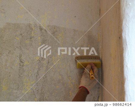 copy space on a texture wall in a room with a major overhaul and a gloved hand with a bush applying a wet layer of primer to the surface, priming the wall with mortar manually during renovation copy space on a texture wall in a room with a major overhaul and a gloved hand with a bush applying a wet layer of primer to the surface, priming the wall with mortar manually during renovation 98662414
