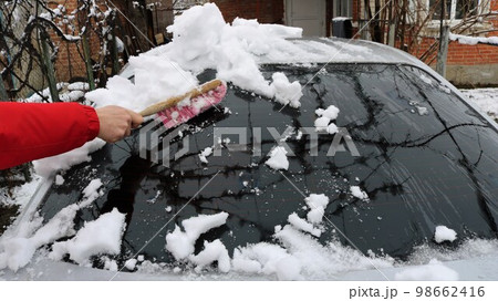 brushing the windshield of a car with a brush after a snowfall, eliminating the consequences of a snow storm when using personal transport at home, a man cleans a car window from snow with a brush brushing the windshield of a car with a brush after a snowfall, eliminating the consequences of a snow storm when using personal transport at home, a man cleans a car window from snow with a brush 98662416