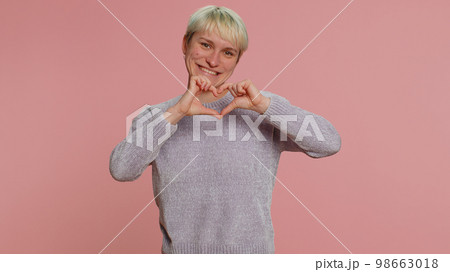 Smiling pretty woman makes heart gesture demonstrates love sign expresses good feelings and sympathy Smiling pretty woman makes heart gesture demonstrates love sign expresses good feelings and sympathy 98663018