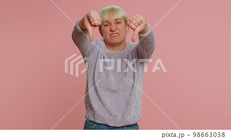 Upset woman in white sweater showing thumbs down sign gesture, disapproval, dissatisfied dislike 98663038
