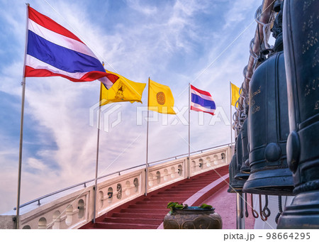 Thai national, buddhist and Thai Royal flags at red staircase and bells at blue sunny sky.  98664295