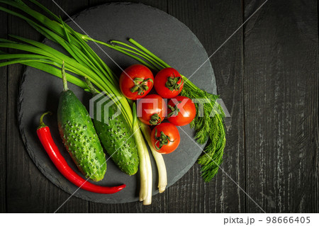 Big set for fresh vegetable salad. Red tomatoes and green young onions with cucumber on a vintage brown plate 98666405