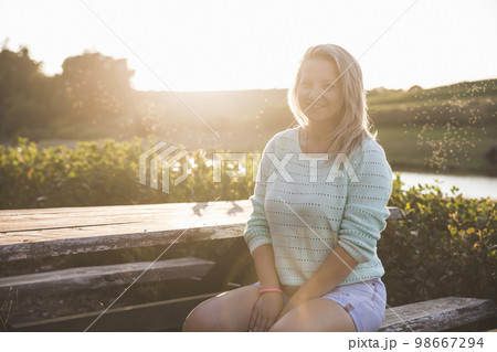blonde girl sitting at sunset at the wooden table near the lake 98667294
