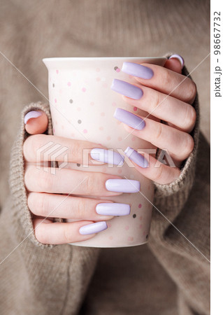 Girl's hands with delicate purple manicure holding a cup of tea. 98667732