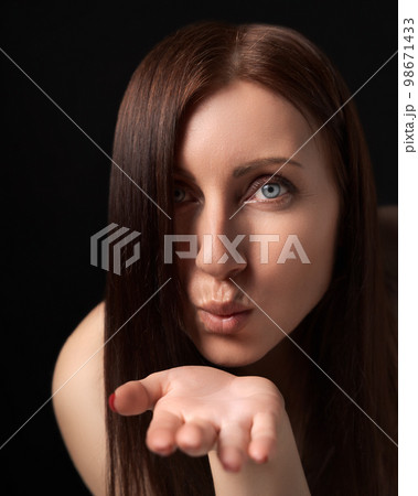 Woman blowing lips sending air kisses over palm to boyfriend, flirting - just for you. 40-year-old Caucasian ethnicity woman with long hair covering one eye showing love and looking at camera. Woman blowing lips sending air kisses over palm to boyfriend, flirting - just for you. 40-year-old Caucasian ethnicity woman with long hair covering one eye showing love and looking at camera. 98671433