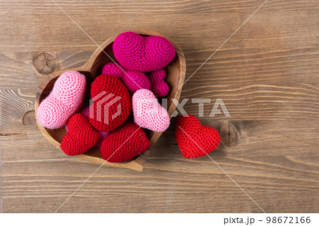Multicolored pink knitted hearts in a wooden bowl in the shape of a heart on a wooden background. Happy Valentine's Day, Mother's Day and birthday greeting card. Multicolored pink knitted hearts in a wooden bowl in the shape of a heart on a wooden background. Happy Valentine's Day, Mother's Day and birthday greeting card. 98672166