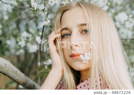 Blonde girl on a spring walk in the garden with cherry blossoms. Female portrait, close-up. A girl in a pink polka dot dress. Blonde girl on a spring walk in the garden with cherry blossoms. Female portrait, close-up. A girl in a pink polka dot dress. 98672226