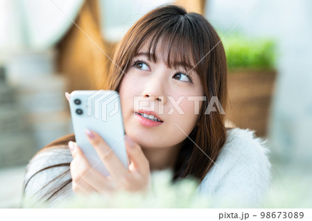 寝転んでスマホを使う若い女性 98673089