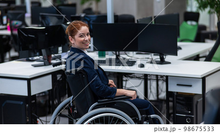 Caucasian smiling woman in wheelchair at work desk.  98675533