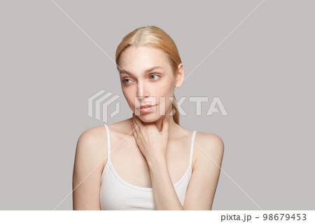 Pensive gorgeous woman touching her neck on grey background. Beauty, cosmetics, skincare, glamour Pensive gorgeous woman touching her neck on grey background. Beauty, cosmetics, skincare, glamour 98679453