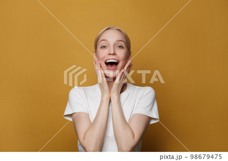 Portrait of cheerful surprised lady. Pretty woman posing against yellow studio wall background Portrait of cheerful surprised lady. Pretty woman posing against yellow studio wall background 98679475