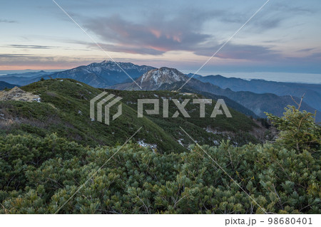 晴天の下で長野と岐阜の県境の西穂高岳稜線から見るアルプスの稜線　朝焼けする北アルプスの山々 98680401