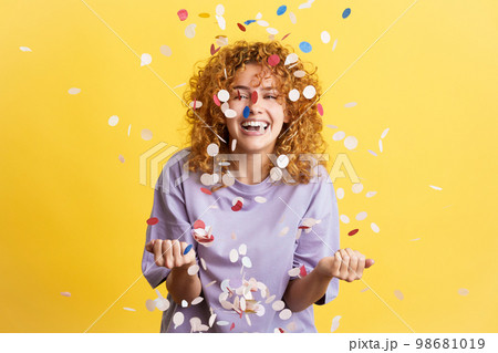 Cheerful woman surrounded by confetti in the air Cheerful woman surrounded by confetti in the air 98681019