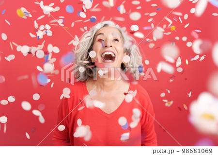 Cheerful mature woman surrounded by confetti in the air 98681069