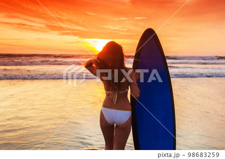 Surfing surfer girl looking at ocean sunset Surfing surfer girl looking at ocean sunset 98683259