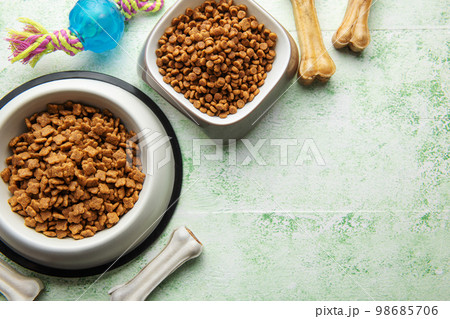 A bowl with dog food, dog treats and toys on a wooden floor. 98685706