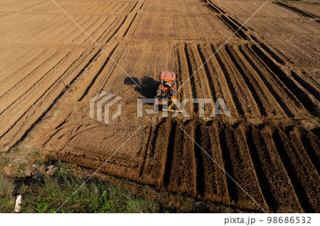 Aerial view of fields and agricultural parcels. Farmer in tractor preparing land with seedbed cultivator as part of pre seeding activities in early spring season of agricultural works at farmlands. Aerial view of fields and agricultural parcels. Farmer in tractor preparing land with seedbed cultivator as part of pre seeding activities in early spring season of agricultural works at farmlands. 98686532
