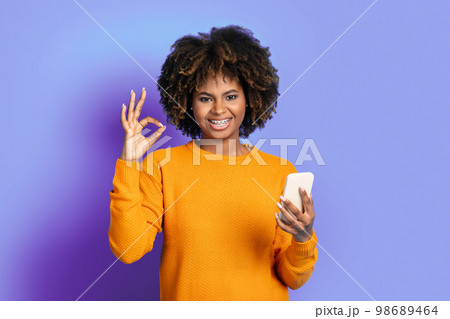 Positive african american lady using smartphone, showing okay gesture Positive african american lady using smartphone, showing okay gesture 98689464