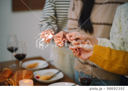 Cheerful friends enjoying home Birthday holiday party. Asian Friends hold lights with sparkling Sparkler celebrating Christmas or New Year eve party. 98692392