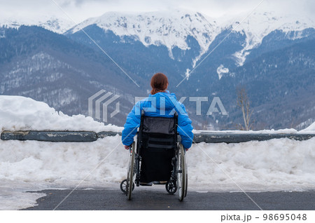 Rear view of a woman in a wheelchair travels in the mountains in winter. 98695048