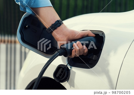 Closeup progressive businessman plugs charger plug from charging station to EV. Closeup progressive businessman plugs charger plug from charging station to EV. 98700205