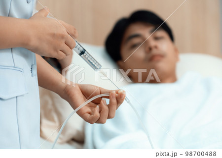 Doctor and nurse inject medicine, dosage into IV tube in sterile recovery room 98700488