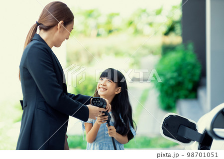 Progressive lifestyle of mother and daughter with EV car and charging station. 98701051