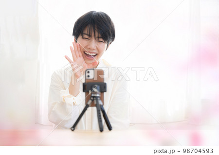 スマホで動画配信をする可愛いらしい女性 春っぽいイメージ スマホで動画配信をする可愛いらしい女性 春っぽいイメージ 98704593