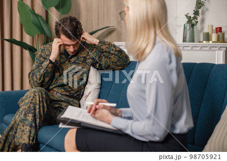 Soldier and psychiatrist sitting on couch during therapy session. Man wearing military uniform. Male warrior with ptds talking to psychiatrist. 98705921