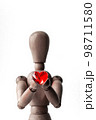 木製のデッサン人形が両手で捧げ持つ赤いハート形のビーズ 98711580