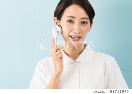 ナース服を着て美顔器の説明をしている若い女性　美容イメージ	 98711976